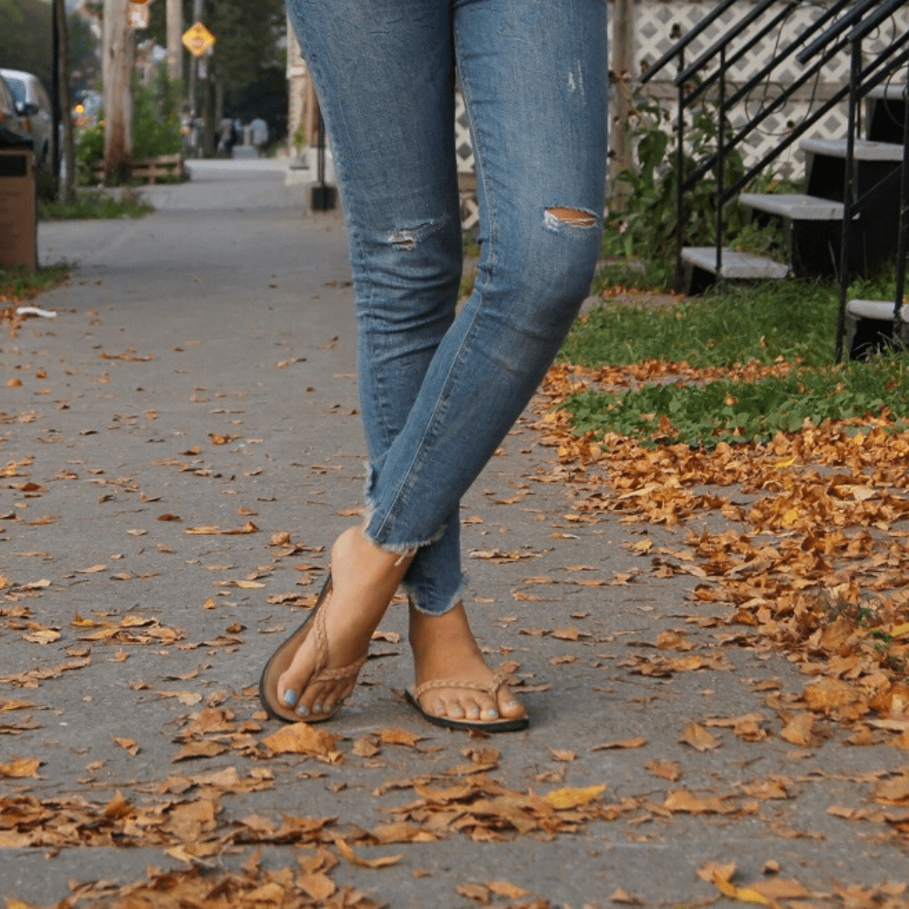Female model wearing The Trenza leather flip flop sustainably made with upcycled tire soles by Brave Soles in caramel color.