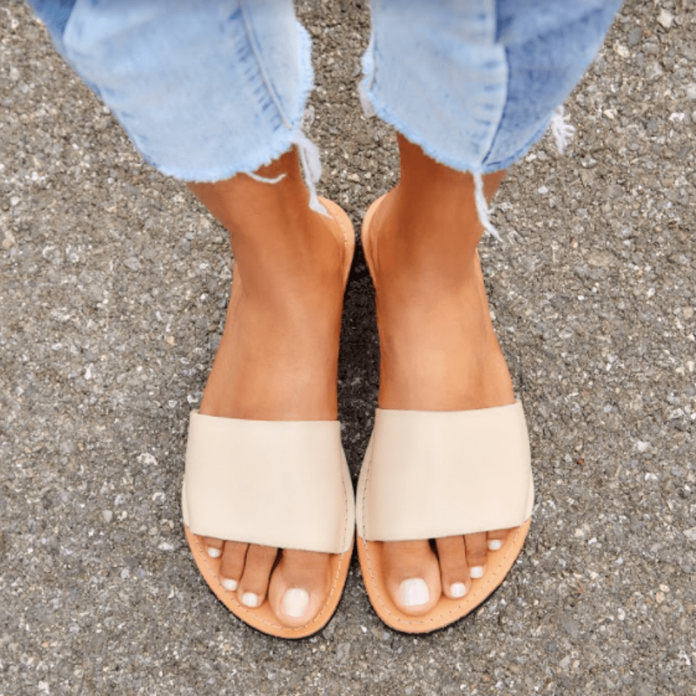 Women's feet in the Linda Women's Leather Slide Sandal in ivory and natural color sustainably made by Brave Soles.